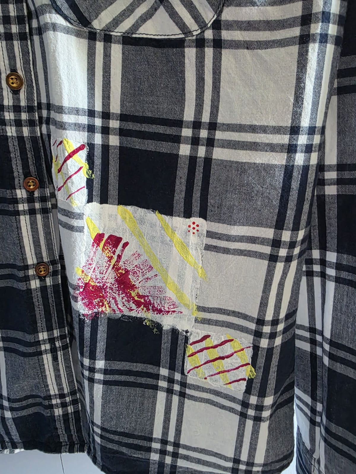 Detalle de pintura geométrica en blanco, amarillo neón y granate sobre camisa de cuadros