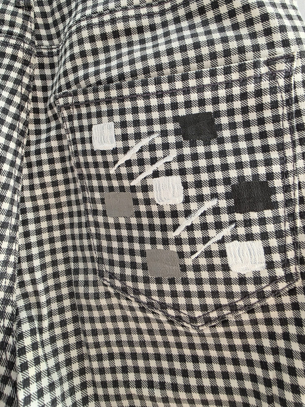 Detalle de un parche artístico gris sobre el tejido de cuadros del pantalón